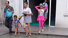 An adult walks with three children.  The children are dressed to go swimming.