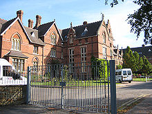 A large brick building with metal gates in front of it; a fence and some trees in the foreground.