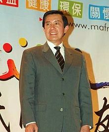 An East Asian man in suit smiling to the crowd