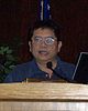 A bespectacled man with a round face speaks behind a podium.