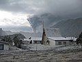 En la imatge es mostra a la ciutat coberta de cendra volcànica i al fons s'observa el volcà.