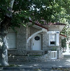 Porch propped up by a stylized wooden beam, windows with wooden lintels and roof ending in prominent eaves