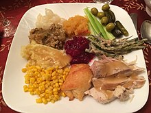 Thanksgiving dinner plate. Clockwise from Turkey in bottom right: dinner roll, corn, mashed potatoes with gravy, stuffing, creamed onions, butternut mash, celery, olives and pickles, and creamed beans, and in the center is cranberry relish. The often large number of components can mean elaborate preparation Thanksgiving dinner plate.jpg