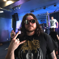 A man in steampunk-style glasses makes the sign of the horns at a rock concert.