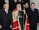 Archbishop Ieronymos II of Athens, Primate of the Church of Greece, wearing a red mantle with gold rivers. Icons of the four evangelists are present on the "tablets," at the clasps of the garment; the icon of Matthew the Apostle is clearly visible in this picture.