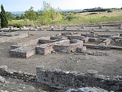 Vestiges de différentes constructions au sol avec des pieds de colonnes et des fondations de forme rectangulaire ou en demi-cercle.