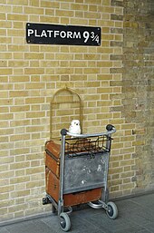 Semn pe care scrie "Platform 9¾" cu jumătate de cărucior de bagaje instalat dedesubt, în interiorul gării King's Cross.