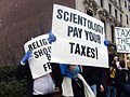 Protester hold signs asking for Scientology to be taxed and that "Religion should be free"