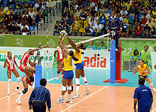 Brazilian and Cuban athletes during a volleyball match wearing the official uniforms of their respective nations. The audience remained watching at the competition venue for the volleyball tournament.