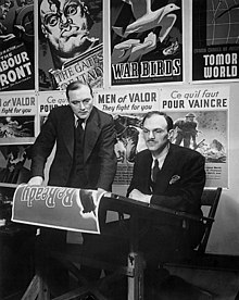 Two men looking at a film poster on a desk against a background of movie posters