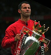 The upper body of a man in a red coat. He has black hair and is holding a large silver trophy.