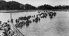 British soldiers wading ashore from landing craft. In the background is a tree lined beach