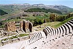 A large stone staircase in the foreground leads down to a ruined building, overlooking a panoramic view of several mountains and valleys.