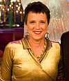 A woman in her late fifties sporting short hair and earrings with the nuclear disarmament logo.