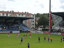 Des joueurs de rugby se tiennent à l'arrêt sur la pelouse d'un stade.