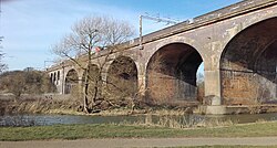 Five of the six arches of a tall bridge across a broad shallow river