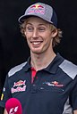 Brendon Hartley in a blue polo and cap with sponsor logos being interviewed