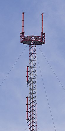 A tall antenna with a goalpost-shaped appendage with two red antennas. Two antennas are mounted lower on the mast.