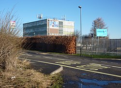 Roadside with bus stop in foreground and slab sided multi storey modern building with large windows behind on a sunny day with a bright blue sky