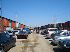 Kereskedők autói parkolnak a konténerekben működő bazárüzletek mögött