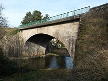 Photographie en couleurs d'un pont en pierre au-dessus d'une rivière, vu depuis la berge.