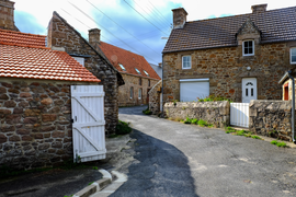 Photographie en couleurs prise à l'entrée d'une voie de circulation. De chaque côté, on voit des maisons construites en pierres apparentes, les toits sont recouverts de tuiles