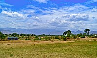 A landscape scenery featuring paddy fields after harvest, in the foreground, with the Podhigai hills as backdrop.