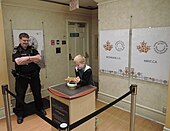 Security officer overseeing a boy with real golden bar in Royal Canadian Mint museum, Ottawa Canada mint museum, Ottawa, Canada.jpg