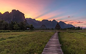 Wooden walkway leading to a hut with straw roof at sunset with colorful sky in Vang Vieng Laos