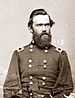 Head and torso of a white man with thick dark hair and a full beard, wearing a double-breasted military jacket with a rectangular patch atop each shoulder.