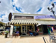 A small building with white walls and a brown and white awning has the sign "Fifth Street Coffee"