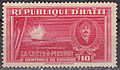 a red postage stamp bearing the words République d'Haïti, with a picture of a ship exploding, as seen from the shore, and an inset image on the right depicting Killick, underneath the images it reads "6 Septembre 1902, La Crête-à-Pierrot, Centimes De Gourde 10