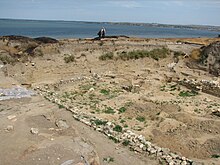 The remains of the wall of a small structure are seen in the foreground, the Sea of Azov is visible in the background.