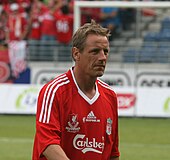 A middle-aged, blond-haired man in a red shirt walks towards the viewer's right at a 45-degree angle.