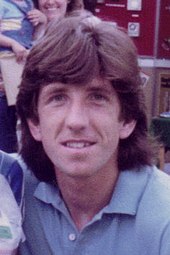 Paul Mariner with shoulder-length hair, wearing an open-necked blue polo shirt