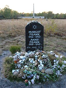 Sebuah Monumen untuk Margot dan Anne Frank yang menampilkan Bintang Daud dan nama lengkap, tanggal kelahiran, dan tanggal kematian masing-masing dari bersaudari tersebut, in white lettering on a large black stone. The stone sits alone in a grassy field, and the ground beneath the stone is covered with floral tributes and photographs of Anne Frank