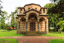 Photographie en couleur d'un petit bâtiment de style néo-roman entouré de tombes