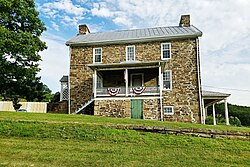 Two story stone house and porch with deciduous tree as seen from grassy yard