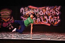 A woman who has black hair tied back and a green T-shirt is swinging herself sideways onto one arm, both feet off the ground.