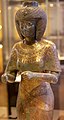 Statuette der Karomama, Hohepriesterin der 22. Dynastie, 9. Jahrhundert vor Chr., Louvre. Das enganliegende Gewand ist aus fein plissiertem Stoff, Schultern und Dekolleté sind mit einem fein gearbeiteten Schmuck aus Gold und Edelsteinen bedeckt.