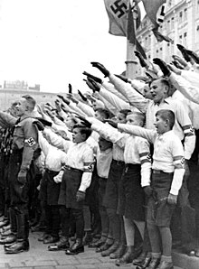 Na imagem estão presentes diversos jovens vestindo uniformes, fazendo a Hitlergruß (saudação nazista)