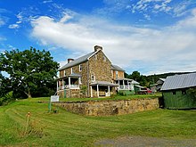 Two story stone house as seen from across a grassy yard, with a stone wall and historical marker in the foreground