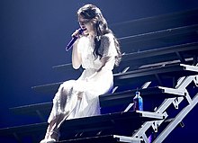 Woman in white dress sat on stairs, singing