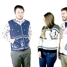 man standing awkwardly with hands in pockets of sweater vest and two people watching from the side