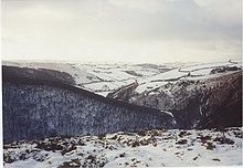 Rounded hills, some wooded, and a river valley are covered in snow.