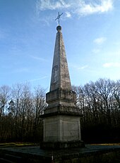 Photographie en couleurs d'un monument en pierre en forme de pyramide très élancée sur un socle cubique.