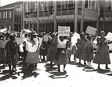 A black and white photo of dozens of protesters, some holding placards.