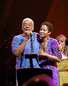 Bill onstage hugging his daughter and speaking into a microphone