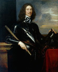 A portrait of a man dressed in black armour. He has long brown hair down to his shoulders and a thin moustache and beard. His left hand is holding a helmet which is resting on a pedestal. His right hand is holding a small pole or scroll