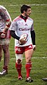 Un joueur de rugby de face, marchant et avec un ballon de rugby dans la main droite.